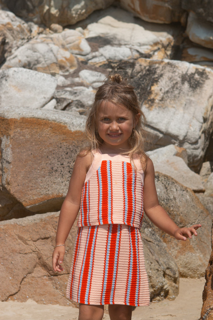 Young girl in a striped top and skirt standing among rocks