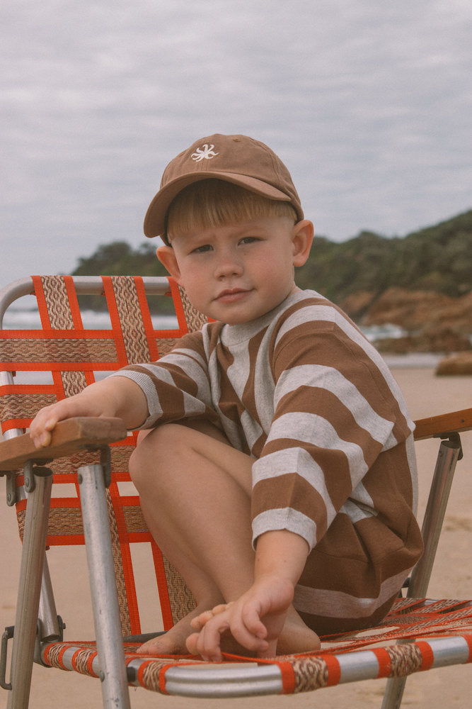 Child sitting on a beach chair at the beach wearing a brown and grey striped romper