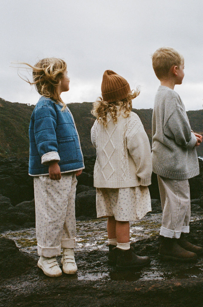 Three children standing on a rocky landscape wearing knitted clothing.