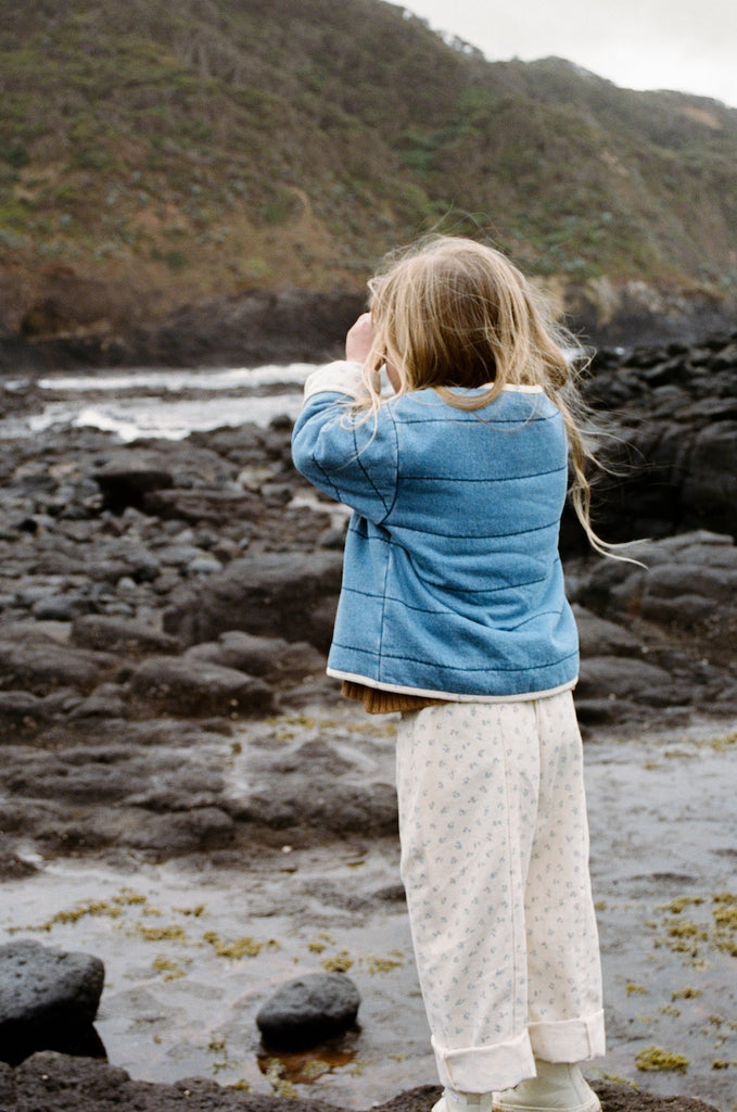 Child wearing a brown knitted top and white floral pants on a brown background