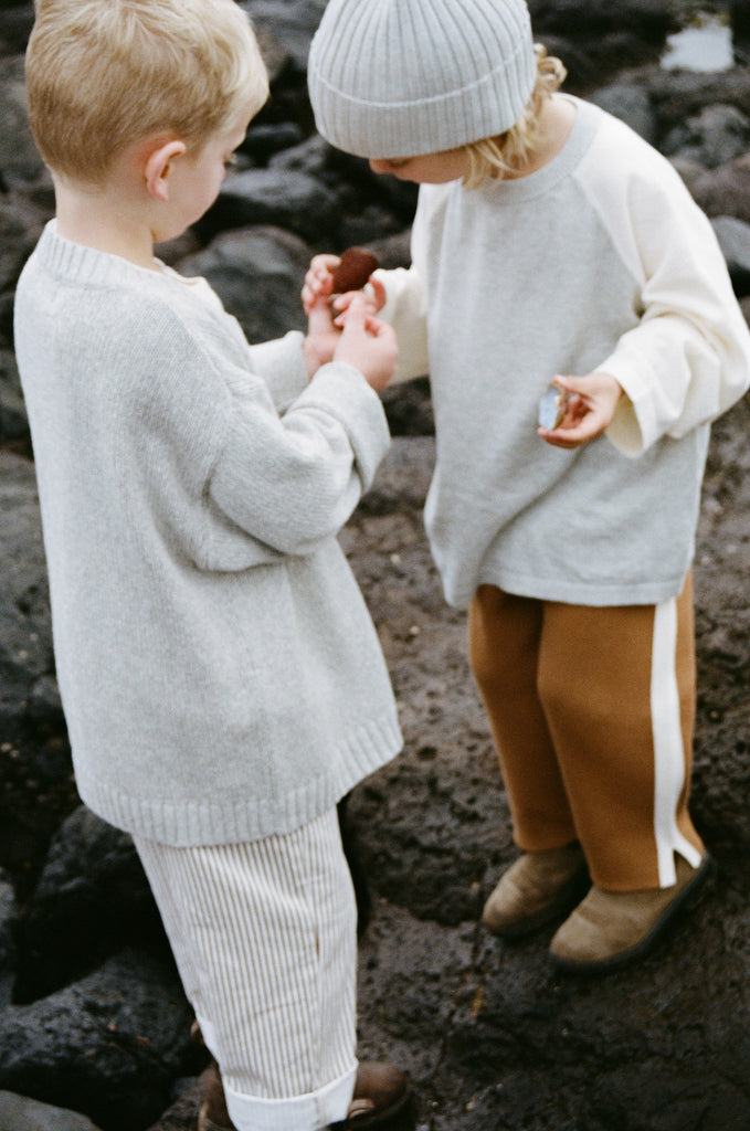 Child wearing a light gray knit hat and a neutral coloured outfit on a brown background on beach