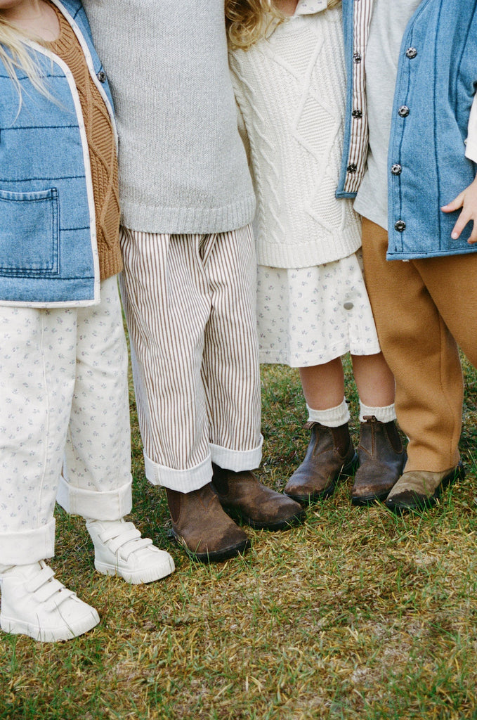 Children wearing boots and various outfits standing on grass