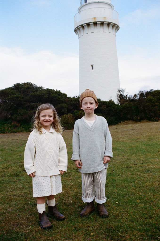 Two children standing in front of a lighthouse on a grassy field.