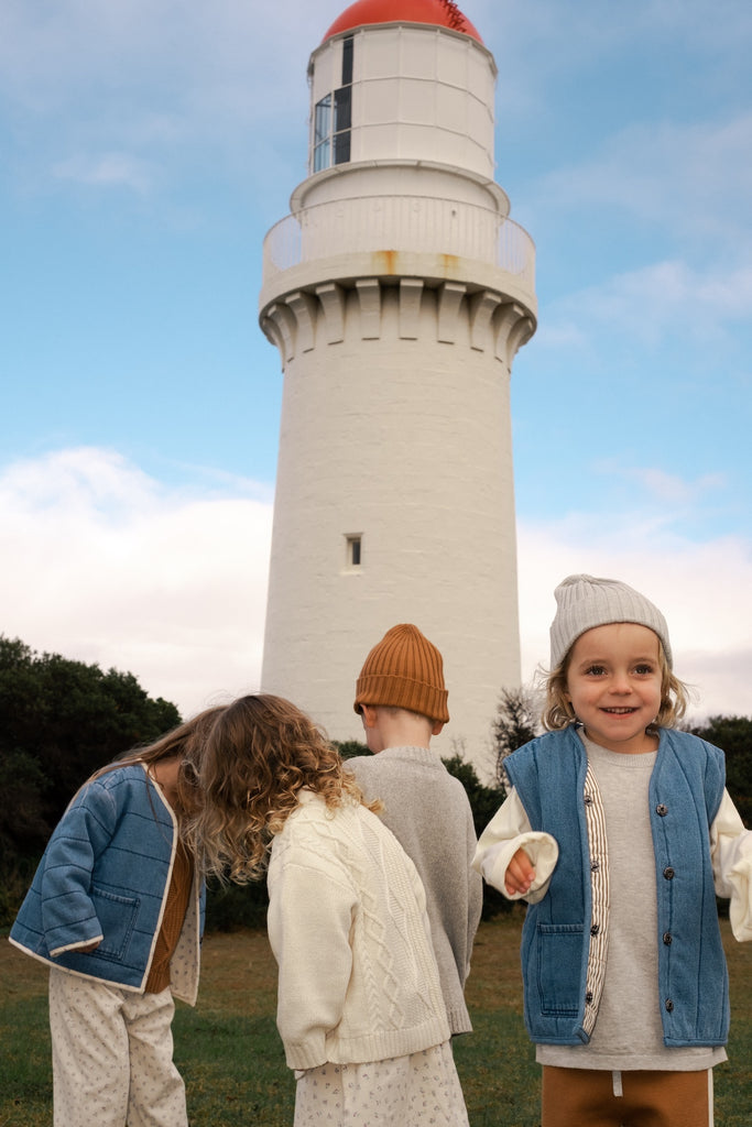 Three children standing in front of a lighthouse wearing grown branded clothing