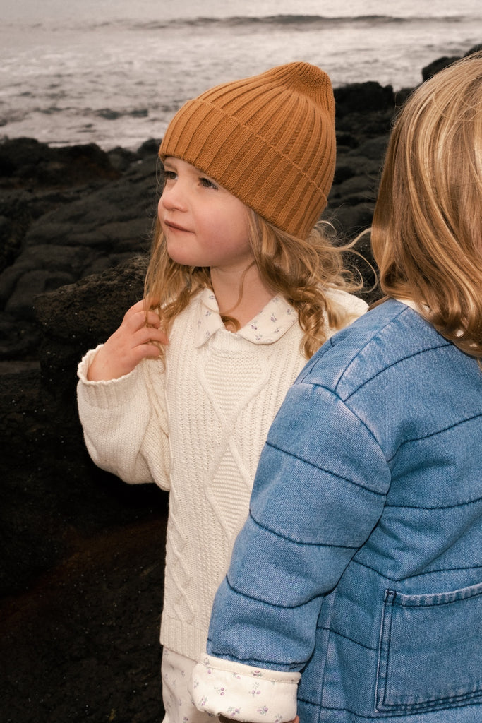 Two children standing on a rocky shoreline with ocean in the background wearing Grown knitwear clothing
