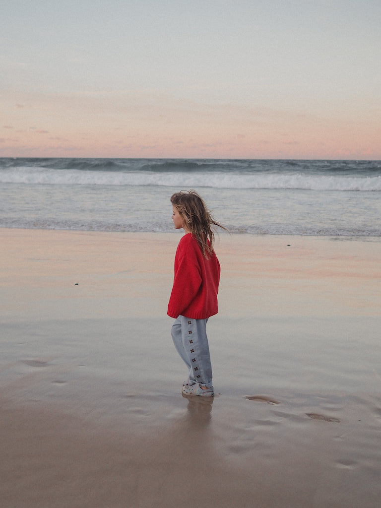 Child in a red jacket standing on a beach at sunset