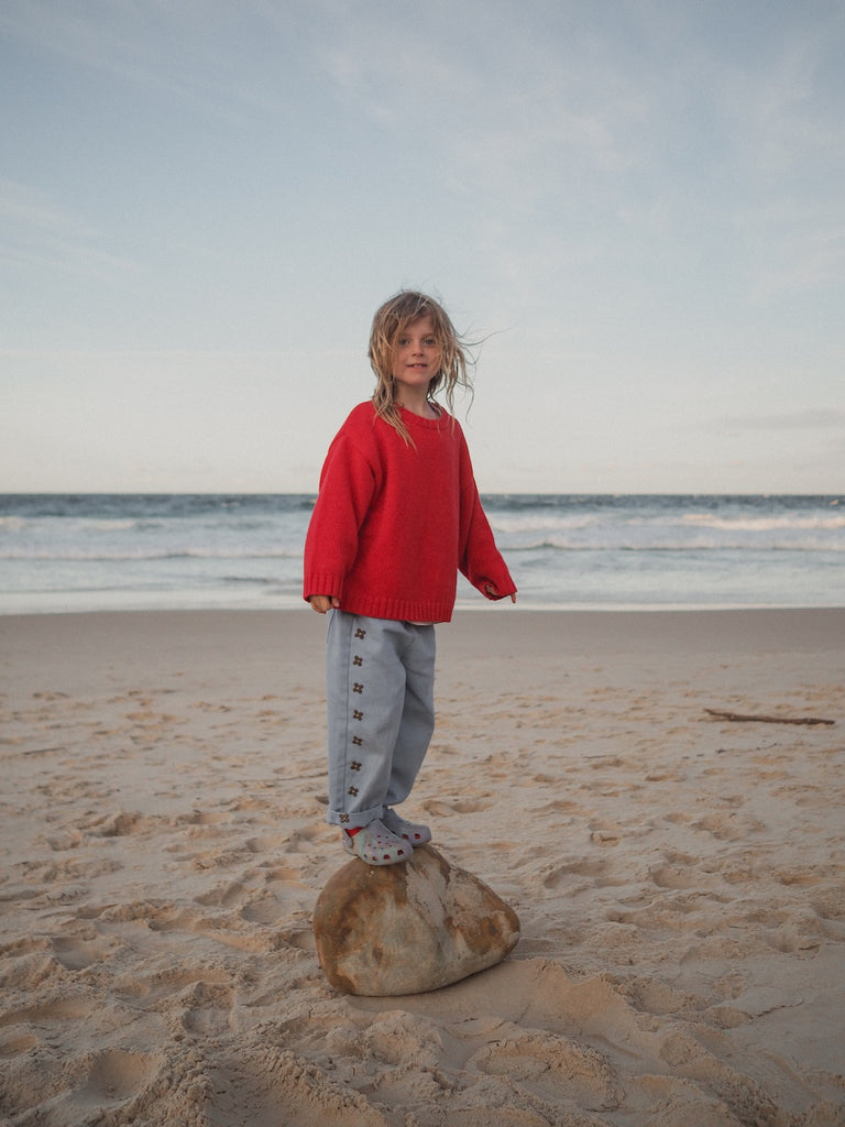 Child in a red sweater standing on a rock at the beach