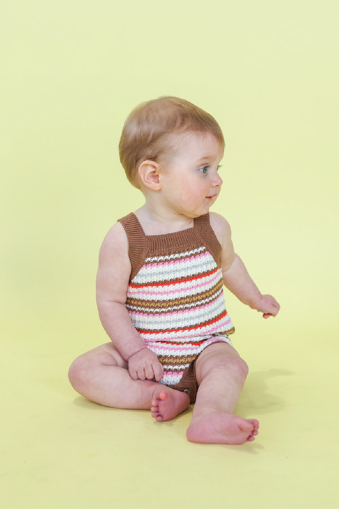 Baby wearing a striped romper sitting on a yellow background