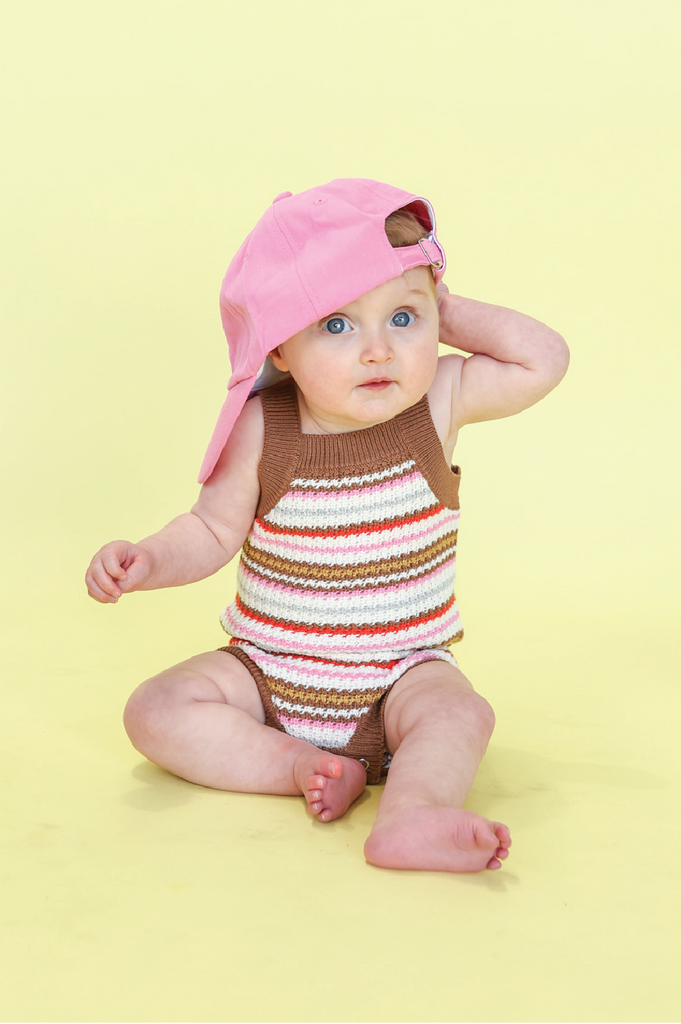 Baby wearing a striped romper sitting on a yellow background