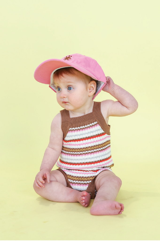 Baby wearing a striped romper sitting on a yellow background