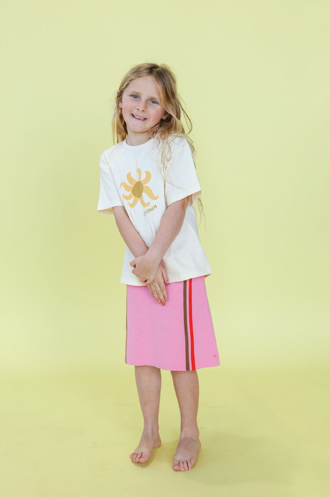 Young girl wearing a white t-shirt with a design and a pink skirt on a yellow background