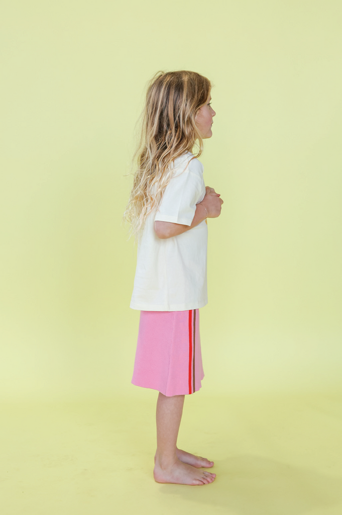 Young girl wearing a white t-shirt with a design and a pink skirt on a yellow background