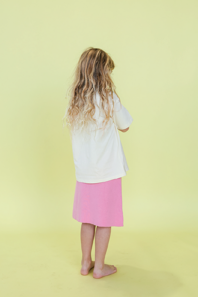 Young girl wearing a white t-shirt with a design and a pink skirt on a yellow background