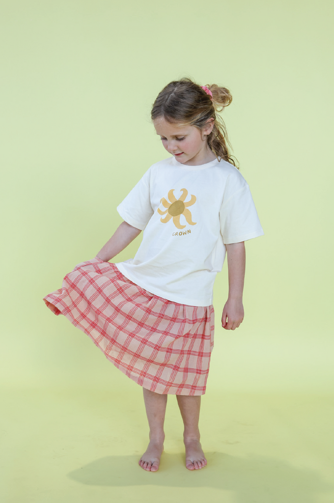 Young girl wearing a white t-shirt with a sun design and a pink checkered skirt on a yellow background