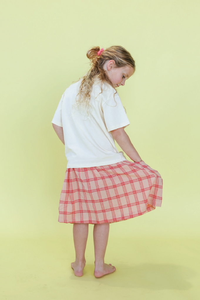 Young girl wearing a white t-shirt with a sun design and a pink checkered skirt on a yellow background