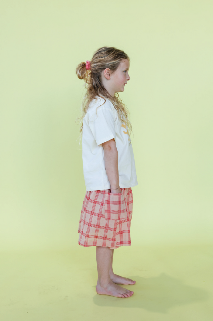 Young girl wearing a white t-shirt with a sun design and a pink checkered skirt on a yellow background