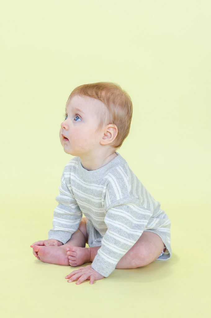 Baby wearing a striped white and grey romper on a yellow background