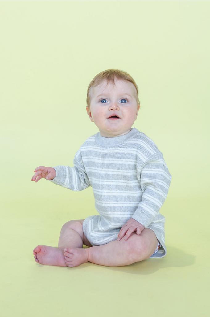 Baby wearing a striped white and grey romper on a yellow background