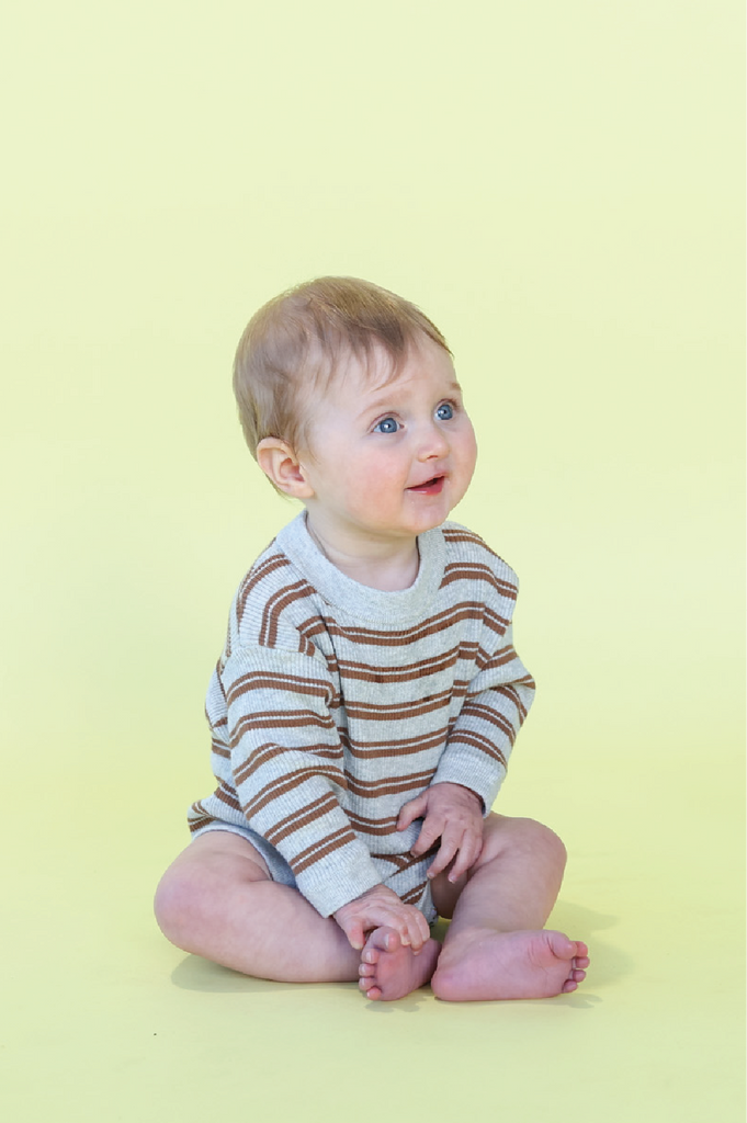 Baby sitting on a yellow background wearing a striped grey and brown romper