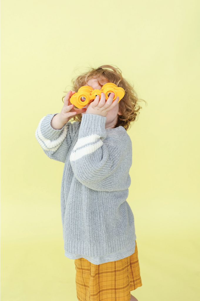 Child wearing grey knit jumper and yellow check shorts and a yellow background