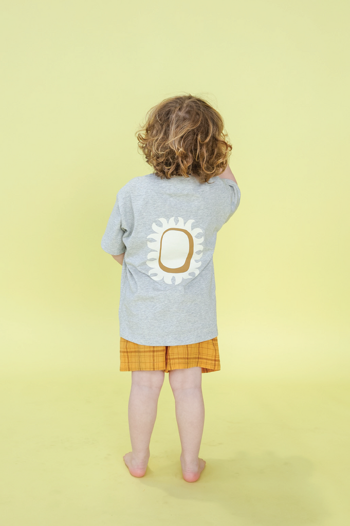 Child wearing a grey shirt and yellow shorts, holding toy binoculars against a yellow background