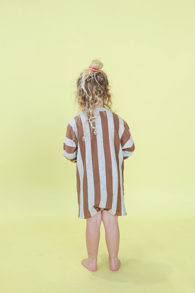 Child wearing a grey and brown striped outfit  against a yellow background

