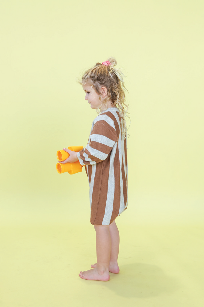 Child wearing a grey and brown striped outfit  against a yellow background