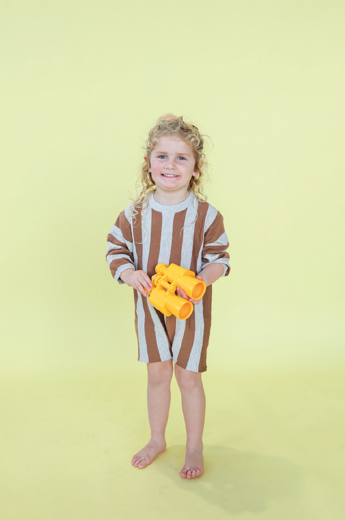Child wearing a grey and brown striped outfit  against a yellow background