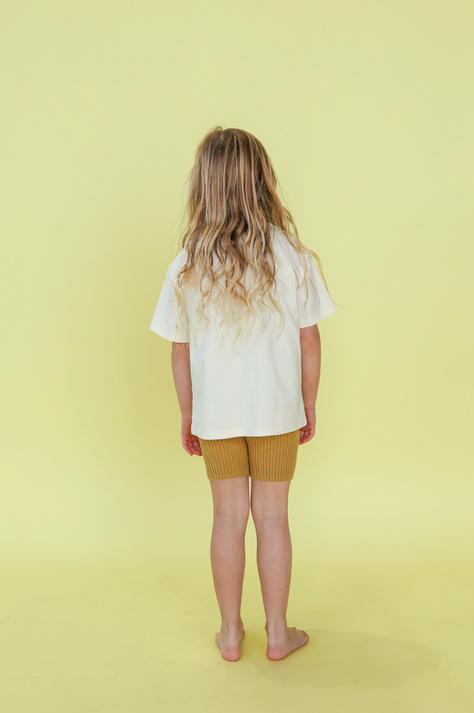 Young girl wearing a white t-shirt with a sun design on a yellow background