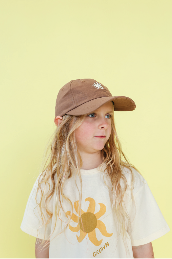 Child wearing a brown cap and white t-shirt with a sun design on a yellow background