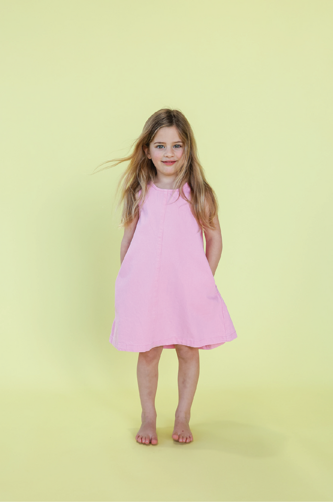 Young girl wearing a pink denim dress against a yellow background