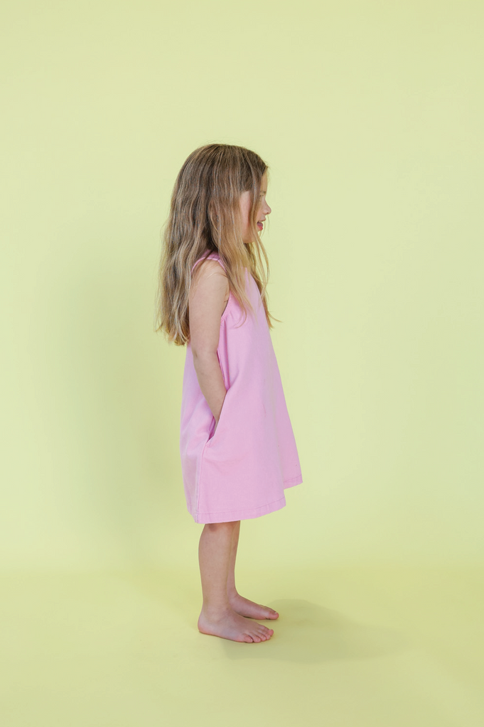 Young girl wearing a pink denim dress against a yellow background