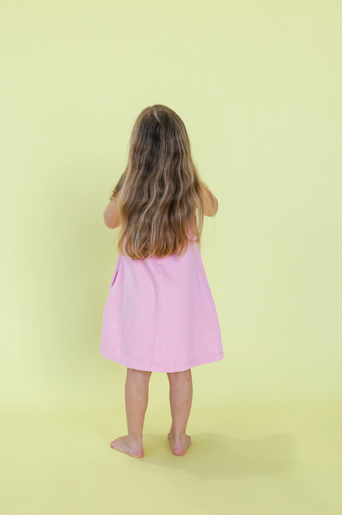 Young girl wearing a pink denim dress against a yellow background