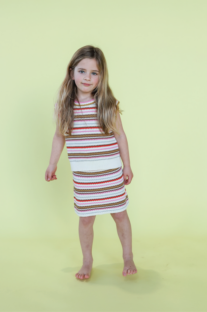 Young child wearing a striped knit vest and skirt on a yellow background
