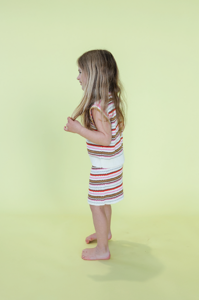 Young child wearing a striped knit vest and skirt on a yellow background