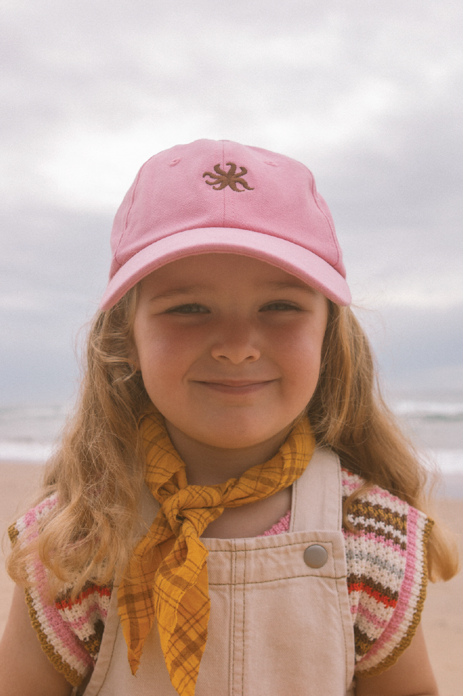Child wearing a pink cap with a logo at the beach