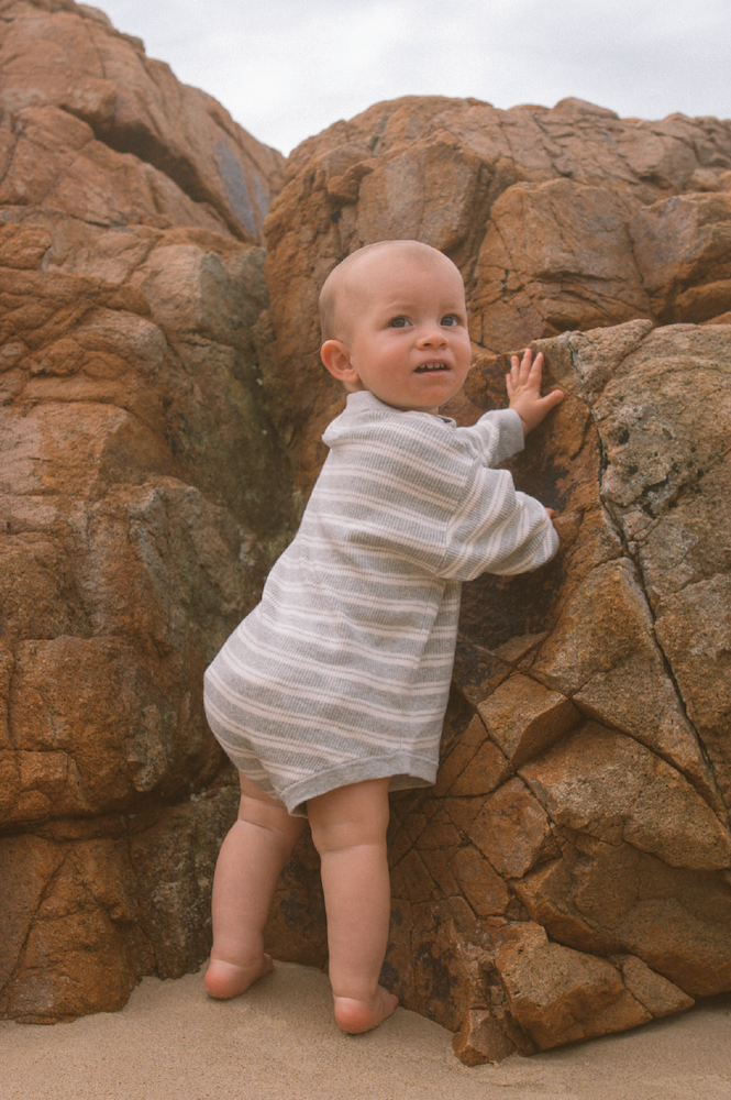 Baby in a striped outfit standing on a rocky beach