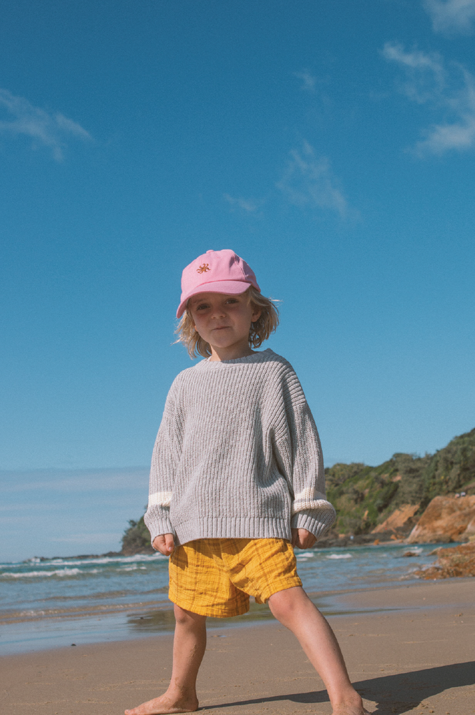 Child wearing grey knit jumper and yellow check shorts at the beach
