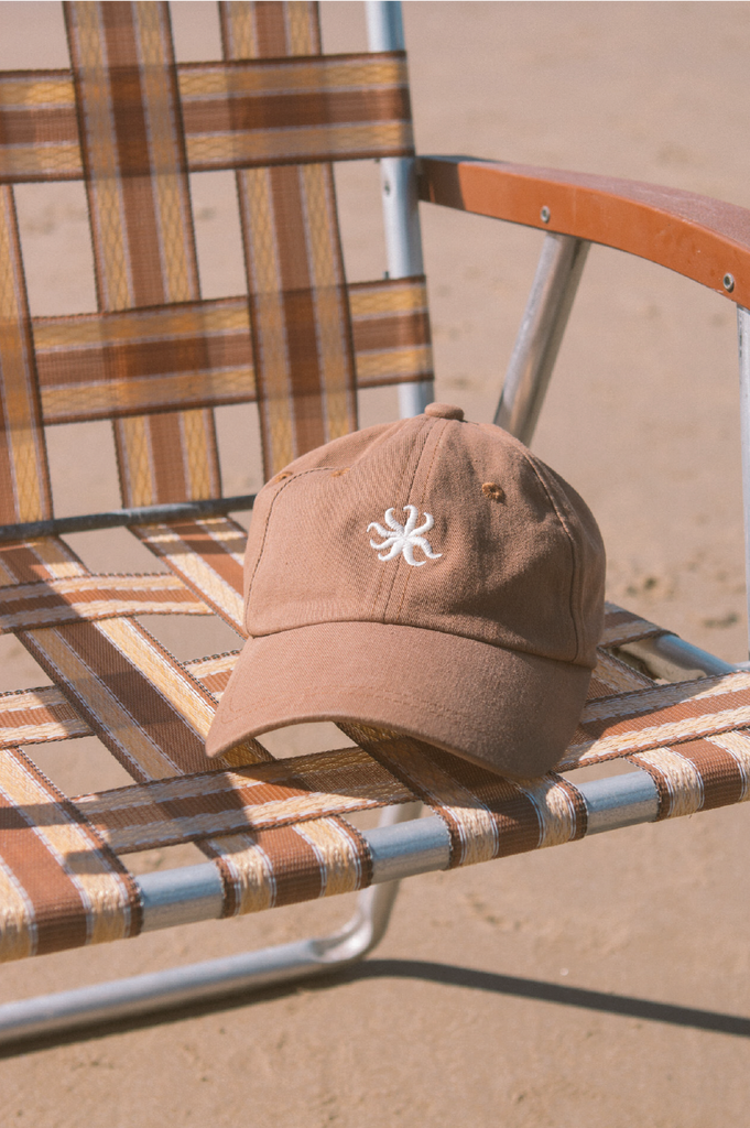 Brown cap with a logo on a plaid chair in a sandy setting