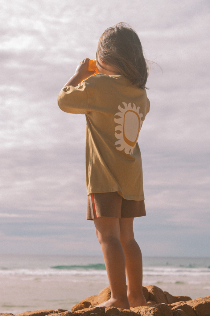 Child wearing a mustard t-shirt with a sun design on a beach