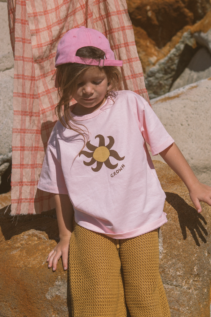 Young girl wearing a pink t-shirt with a sun design sitting on a rock