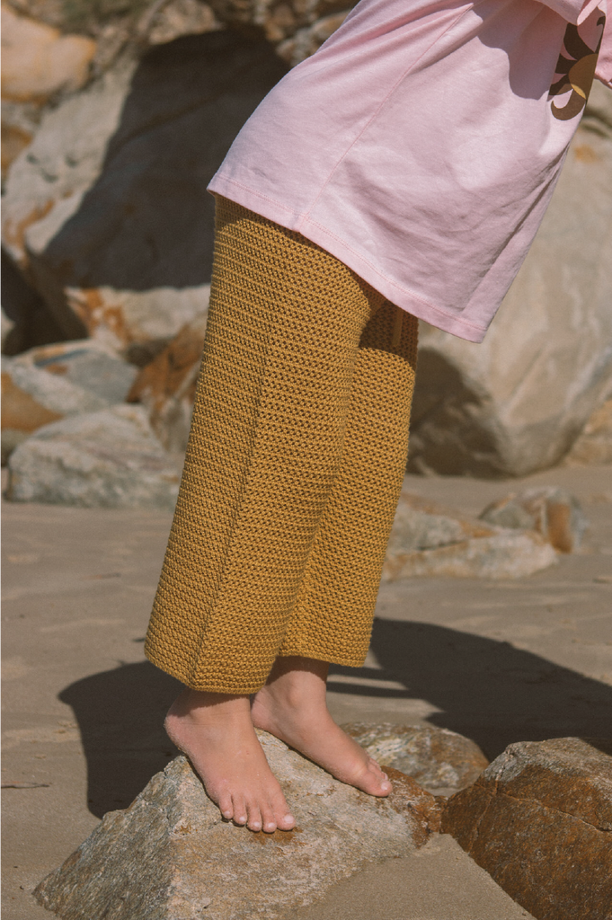 Person wearing mustard yellow pants and a pink top standing on rocks.
