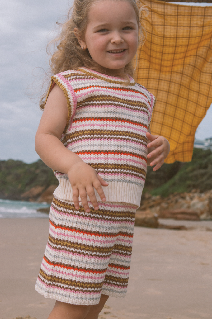 Young child wearing a striped knit vest and skirt on a beach