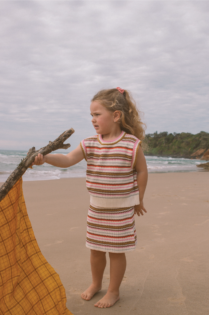 Young child wearing a striped knit vest and skirt on a beach