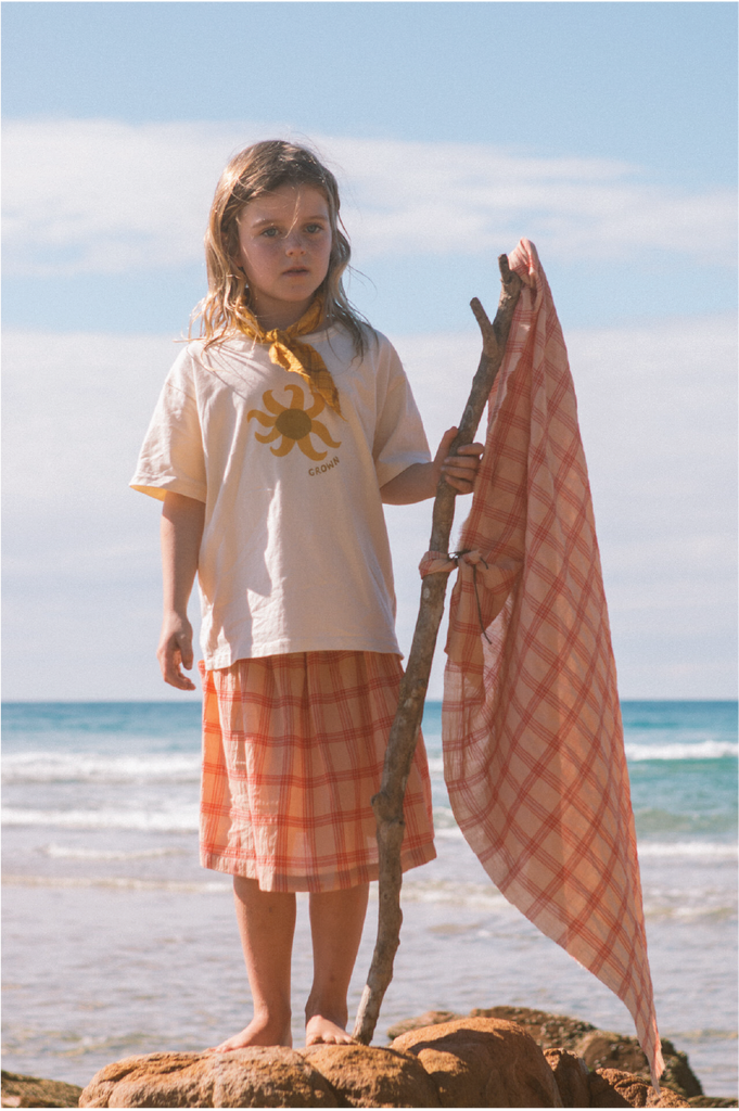 Young girl wearing a white t-shirt with a sun design  and checkered skirt standing on a rock at the beach