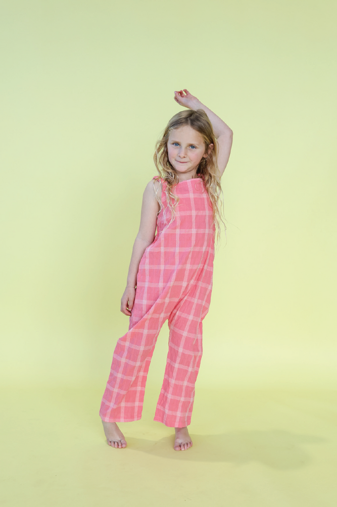 Young girl wearing a pink checkered overalls against a yellow background