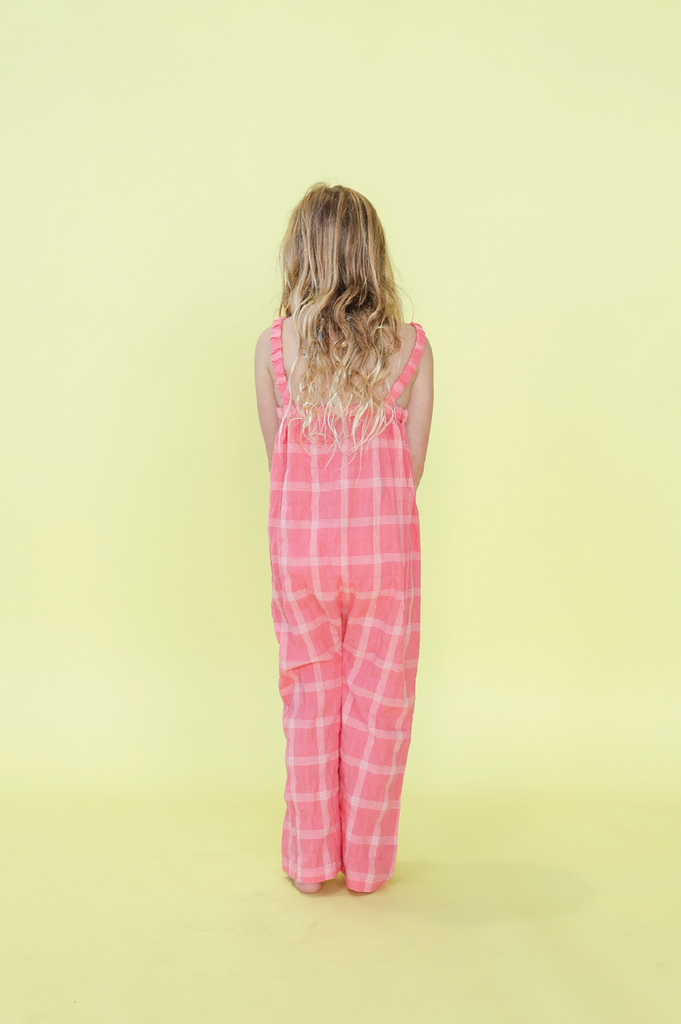 Young girl wearing a pink checkered overalls against a yellow background