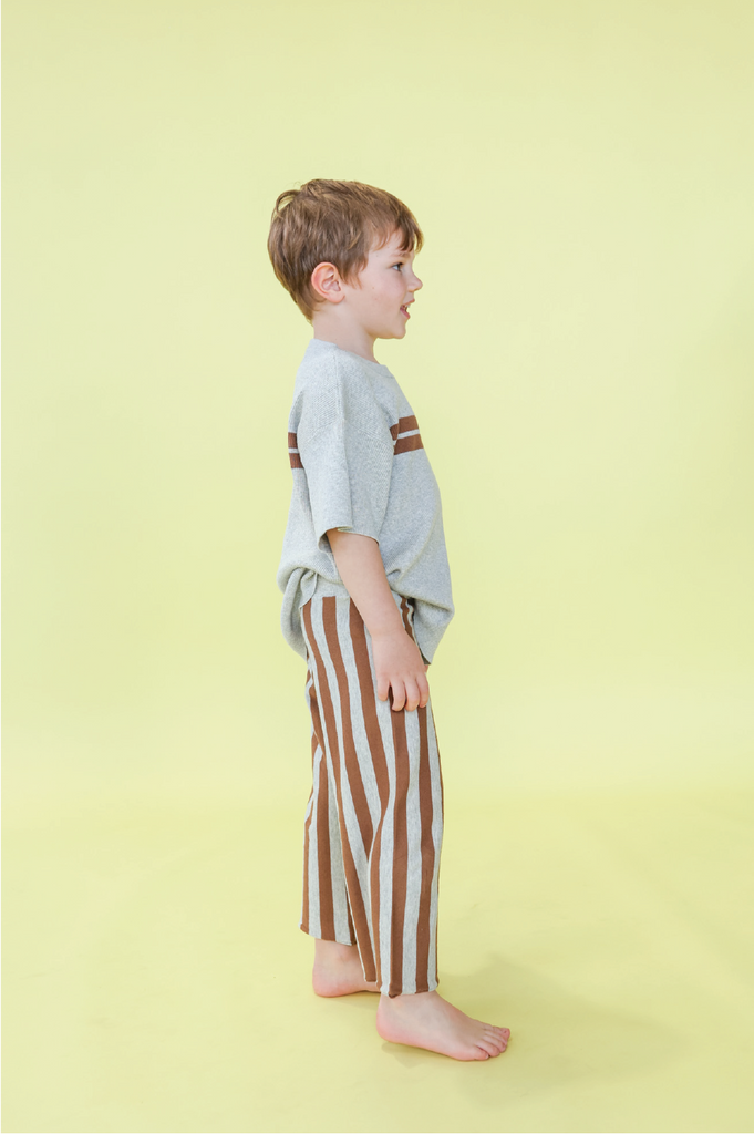 Young boy wearing a grey t-shirt with brown stripes and grey and brown striped pants on a yellow background