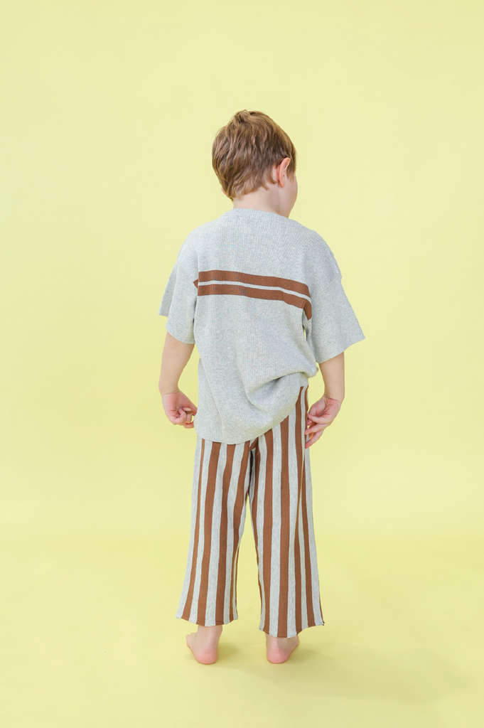 Young boy wearing a grey t-shirt with brown stripes and grey and brown striped pants on a yellow background