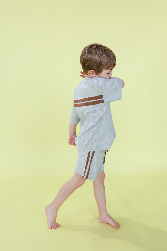 Child wearing a grey t-shirt with brown stripes and grey stripe shorts on a yellow background